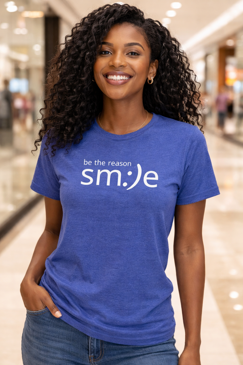 Woman wearing a blue t-shirt with 'be the reason smile' text in a mall setting