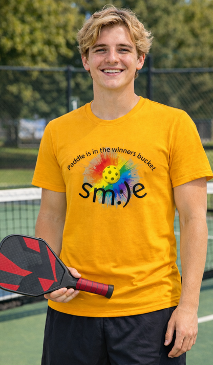 Person wearing a yellow t-shirt with a colorful smiley face design on a pickleball court